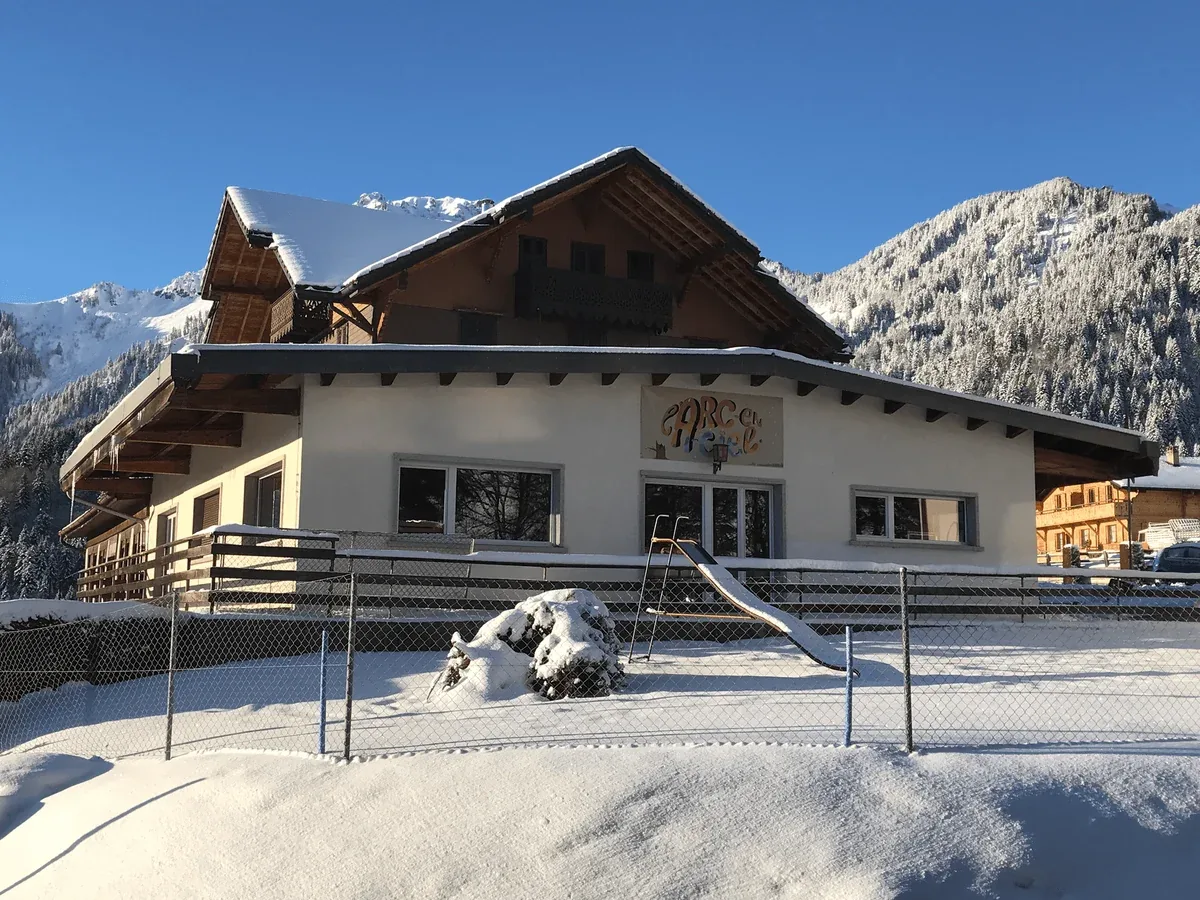 Le chalet Arc-en-Ciel sous la neige, ciel bleu et montagnes enneigées